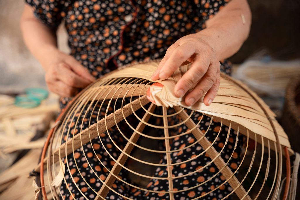 Flechthandwerk in Arbeit: Hände formen einen Korb aus hellem Material.